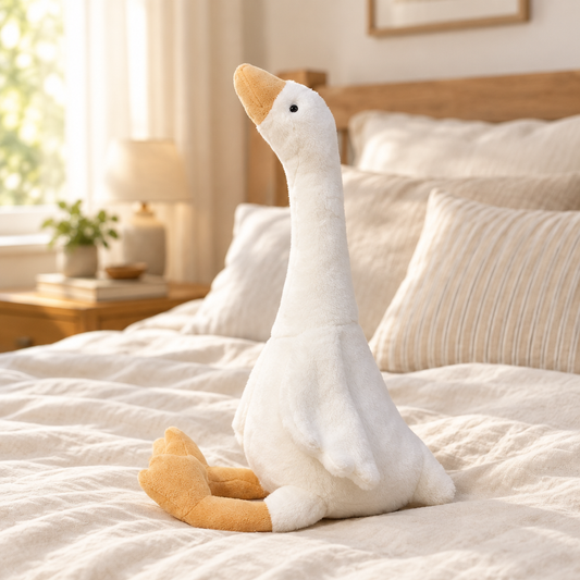 White goose plushie sitting on a bed, turned towards the camera